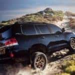 A black 2021 Toyota Land Cruiser is shown from a rear angle driving on a remote trail.