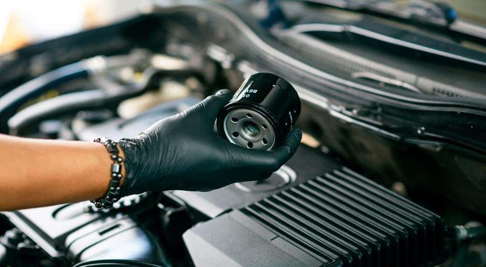 A gloved mechanic is shown holding an oil filter over an engine.