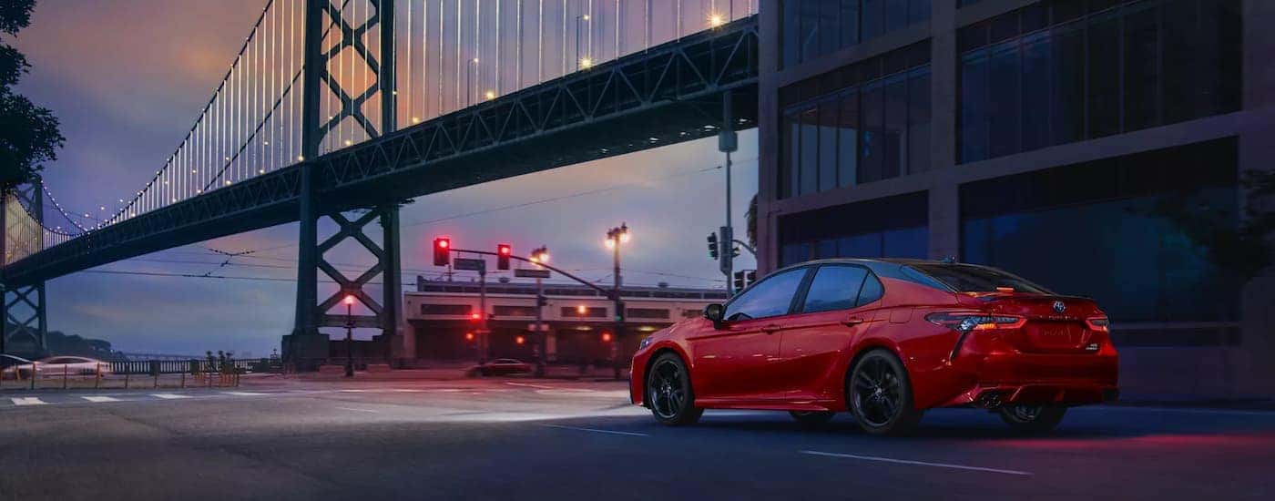 A red 2022 Toyota Camry XSE Hybrid is shown at night with a bridge in the distance.