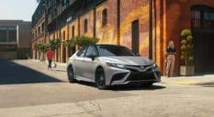 A silver 2022 Toyota Camry XSE Hybrid is shown next to a brick building after visiting a Toyota Camry dealer.