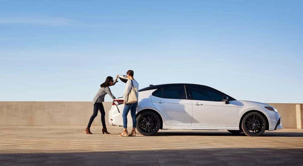 A couple is shown opening the trunk of a white 2022 Toyota Camry XSE.