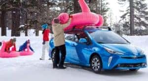 A family is shown sledding near a blue 2022 Toyota Prius AWD after installing new winter tires.