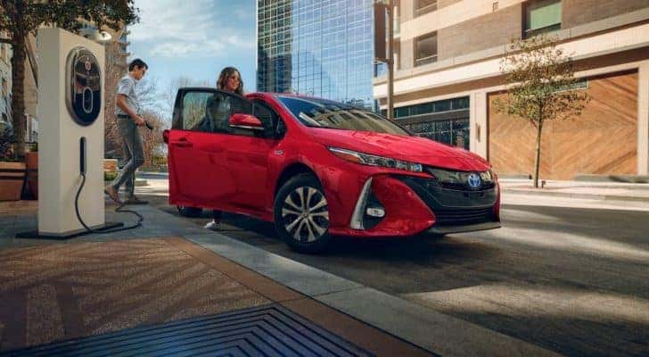 A red 2021 Toyota Prius Prime parked next to an EV charger near a certified pre-owned Toyota dealer.