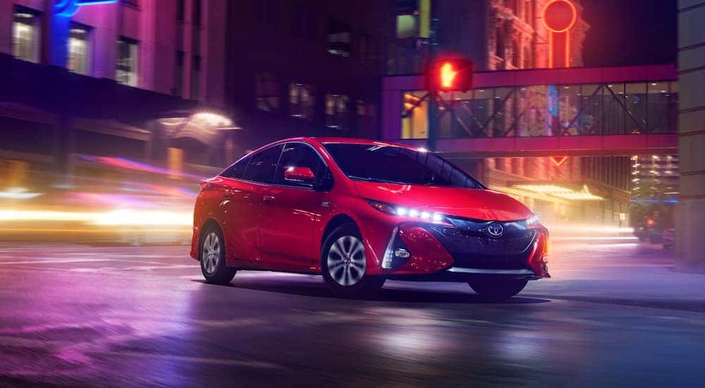 A red 2020 Toyota Prius Prime is shown driving through a city.