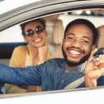 A couple is shown smiling in the front seat of a car while holding a key at a Toyota lease return.
