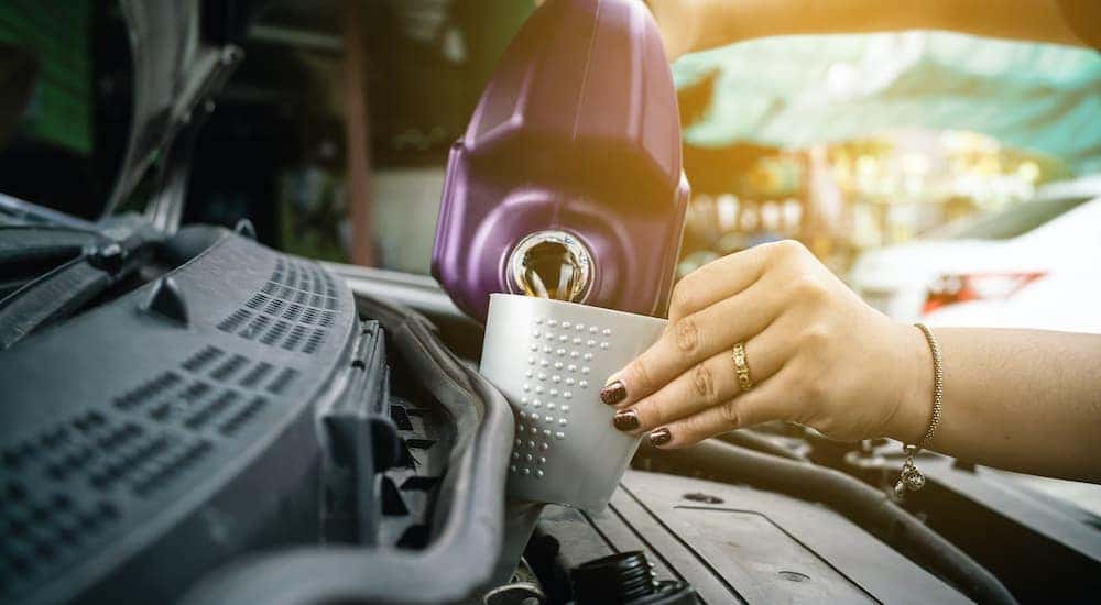 A person is shown pouring oil into their car engine while using a funnel.