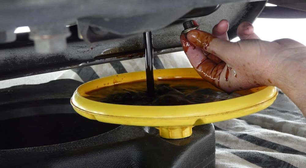 A person is shown draining the oil out of a car into a yellow drip pan.