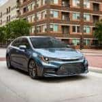 A slate 2022 Toyota Corolla is shown driving on a city street.