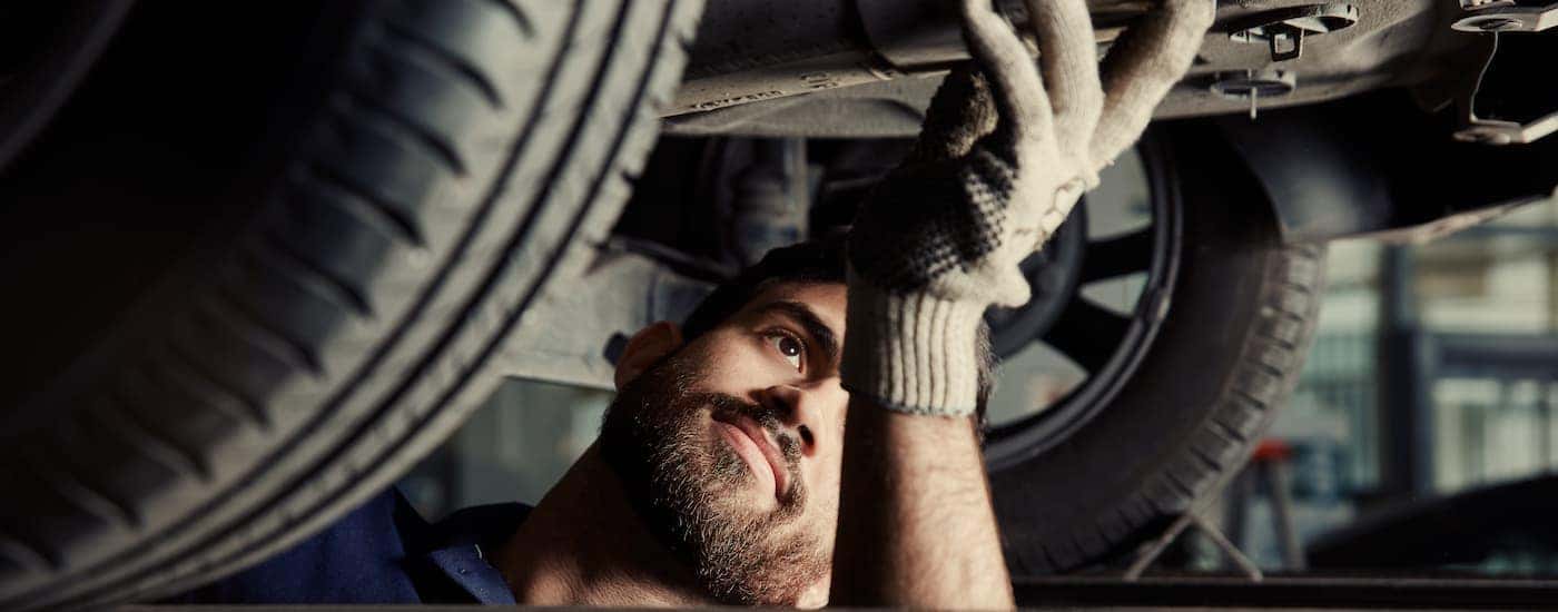 A mechanic is shown looking at the underside of a car at an exhaust shop.