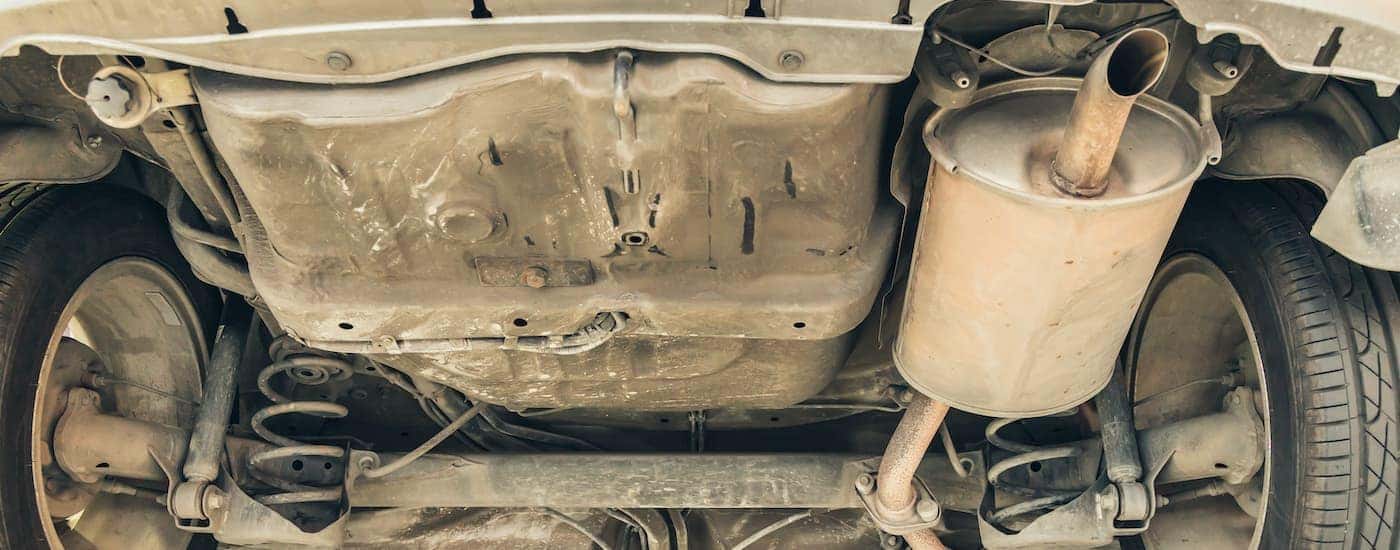 The underside of a car is shown at an exhaust shop.