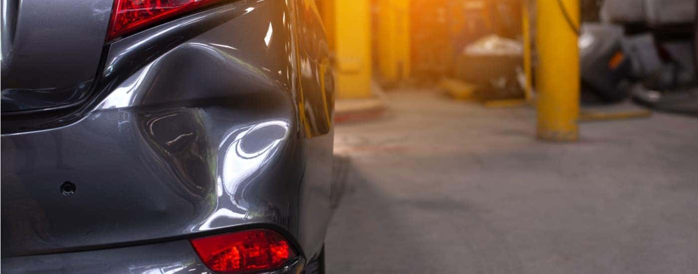 A close up of a dented bumper is shown at an auto collision repair center.