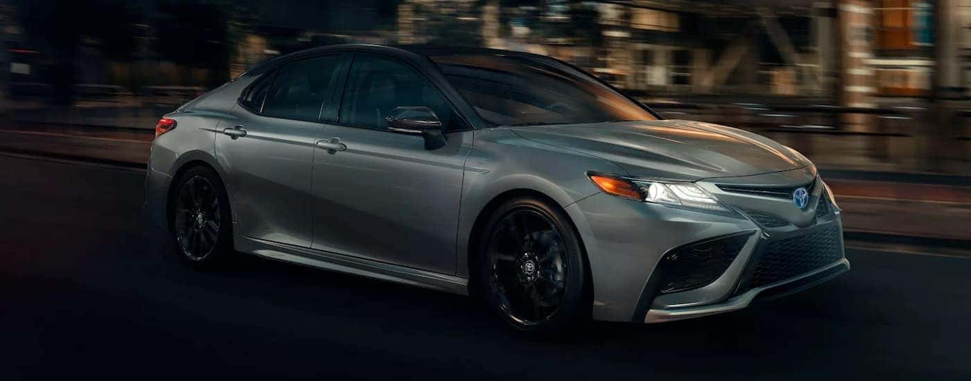 A silver 2021 Toyota Camry XSE Hybrid is shown from the side driving in a city at night.