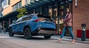 A person is shown walking behind a blue 2022 Toyota RAV4 Hybrid XSE parked on a city street.