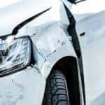 A white car is shown from the front with damage to the driver's side after the driver searched auto collision repairs.