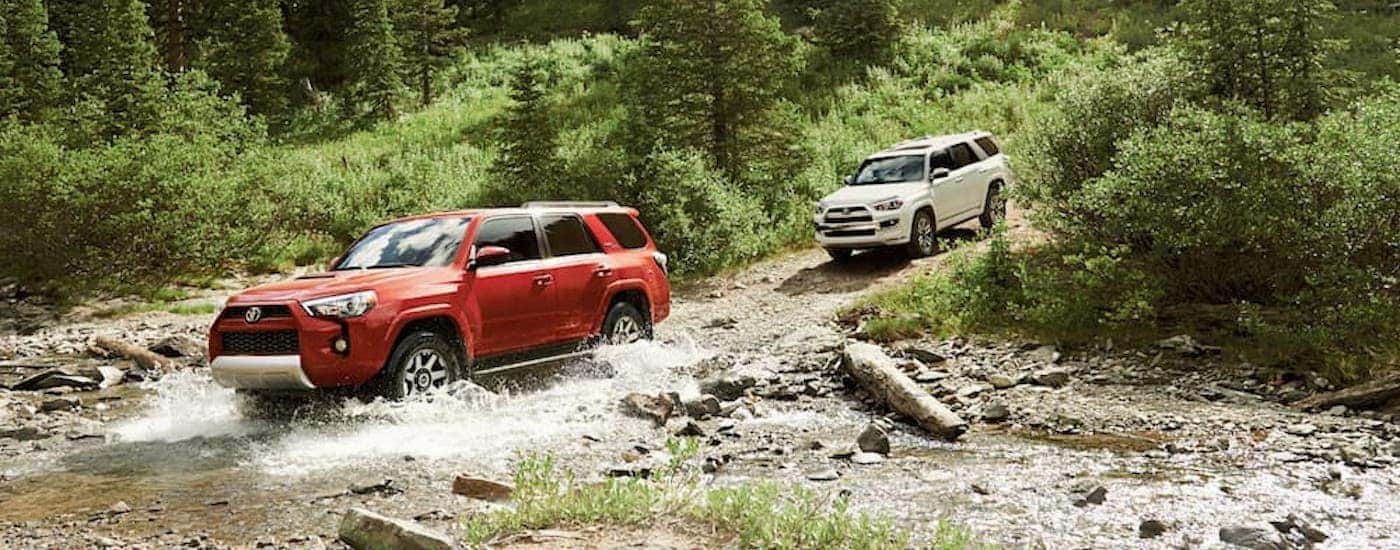 A red and a white 2020 Toyota 4Runner are shown off-roading through a river.