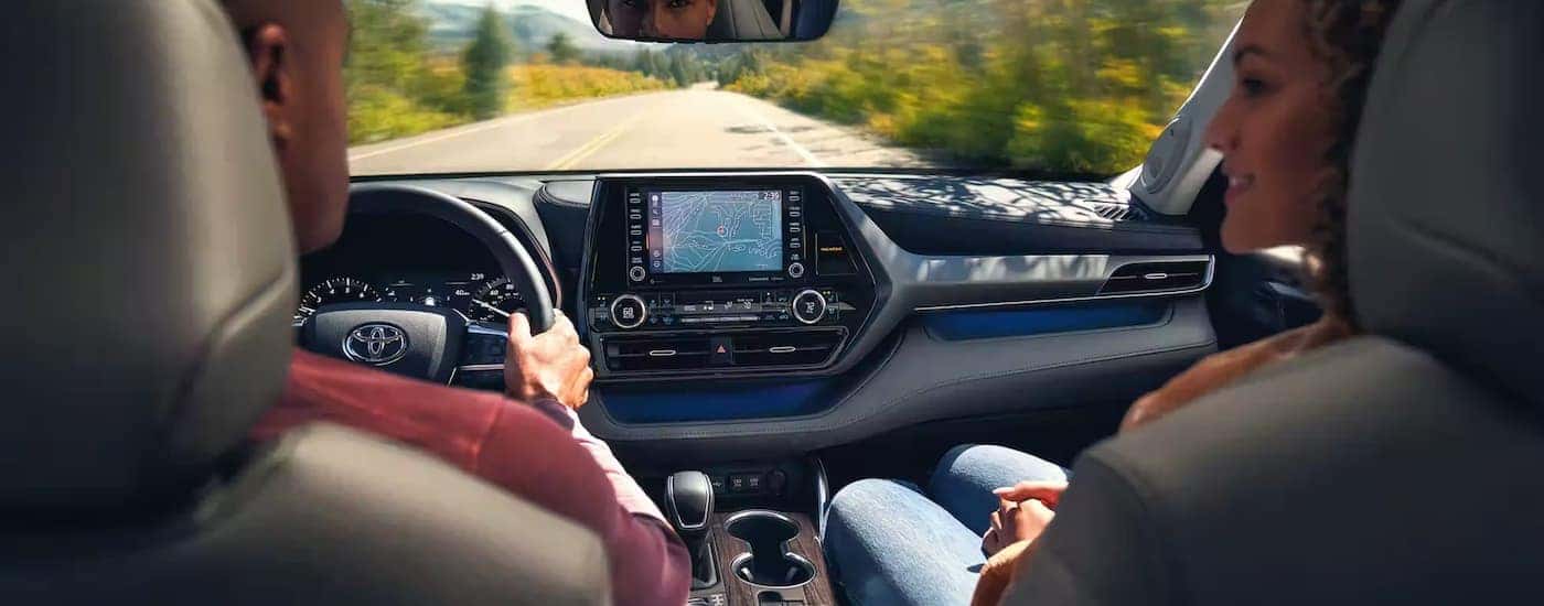 A couple is shown in the front seats of a 2022 Toyota Highlander driving on an open road.