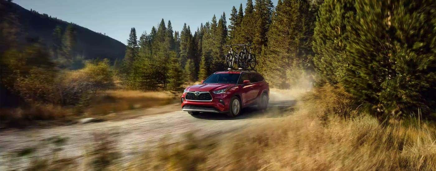 A red 2022 Toyota Highlander is shown driving on a dirt road.