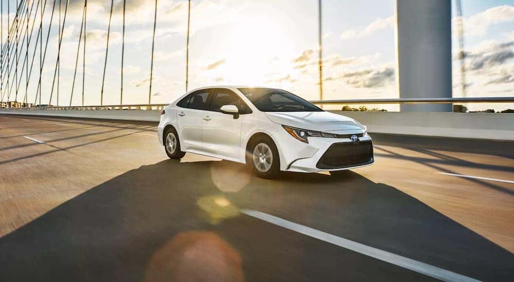 A white 2022 Toyota Corolla Hybrid LE is shown driving to a dealership to value their trade.