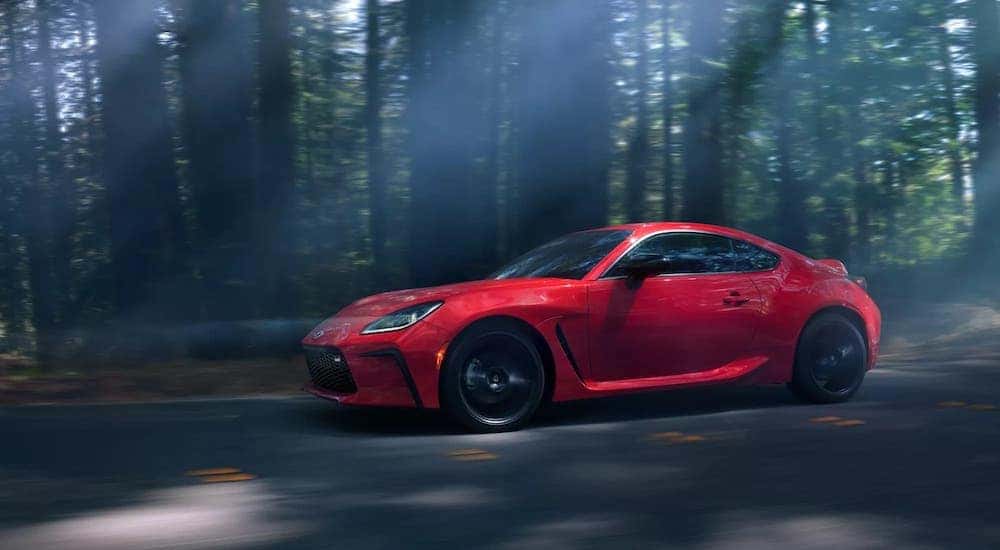 A red 2022 Toyota GR86 is shown driving through a dark forest.
