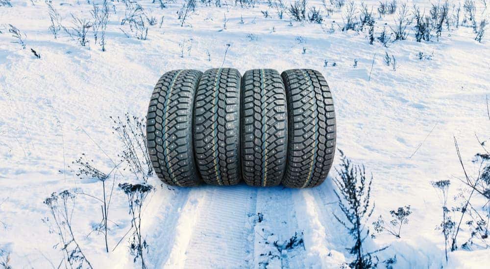 Four winter tires are shown next to tire tracks in snow.