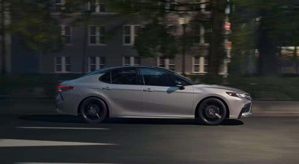 A popular Toyota Camry for sale, a silver 2023 Toyota Camry XSE Hybrid, is shown from the side on a city street.