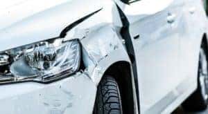 A white car is shown from the front with body damage before heading to an auto body shop near me.