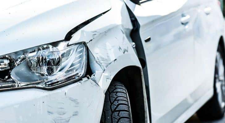 A white car is shown from the front with body damage before heading to an auto body shop near me.