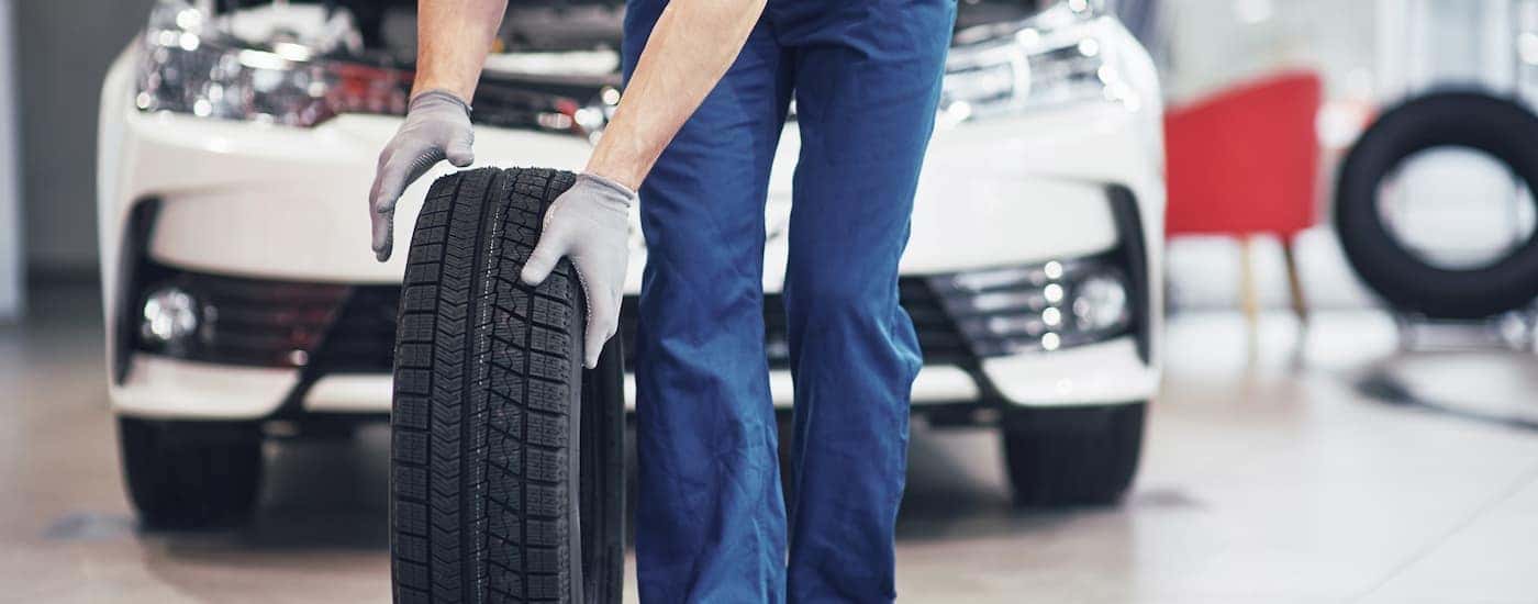 A mechanic is shown rolling a tire near a white sedan at a Toyota service center.