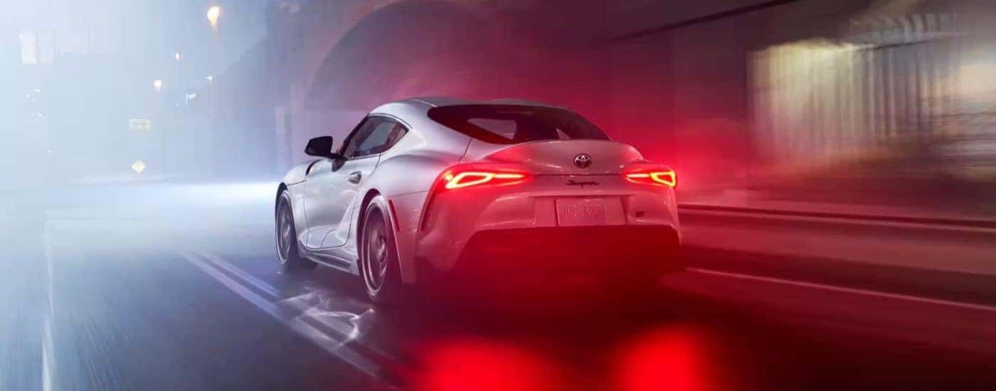 A white 2023 Toyota GR Supra is shown from the rear on a city street at night.