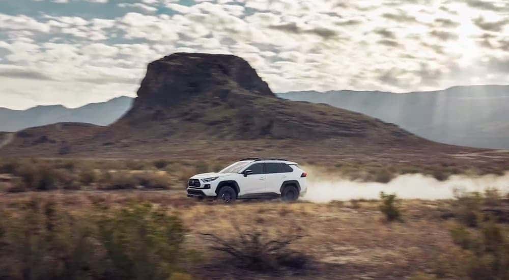 A white 2022 Toyota RAV4 is shown from the side while driving off-road.