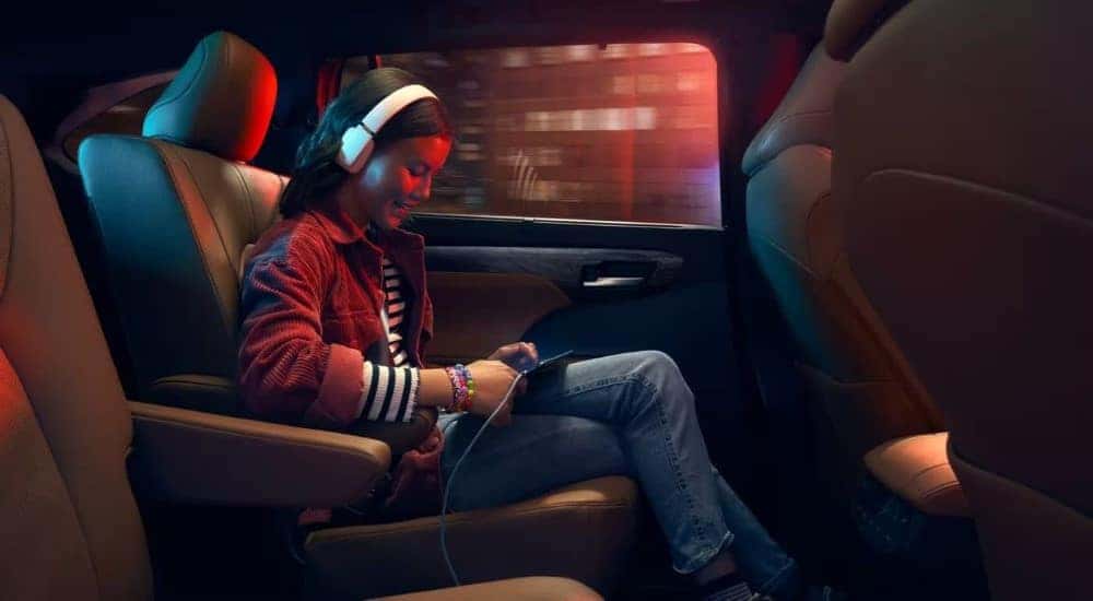 A child is shown with a tablet and headphones in a 2023 Toyota Highlander Hybrid for sale.