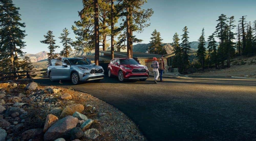A blue 2023 Toyota Highlander Platinum and a red Hybrid Platinum are shown near a cabin.