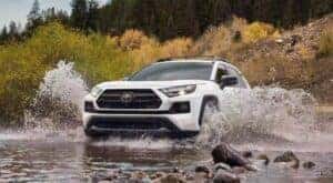 A white 2023 Toyota RAV4 TRD is shown splashing through a river.