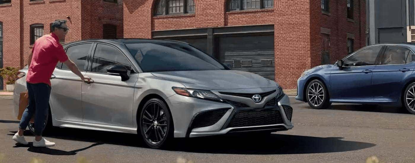 A silver and a blue 2023 Toyota Camry are shown parked on a city street.