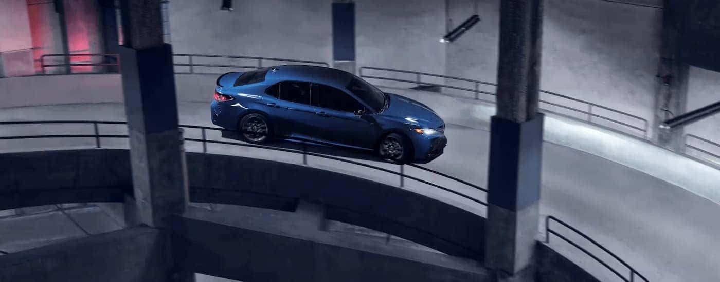A blue 2023 Toyota Camry is shown driving down a winding parking garage ramp.