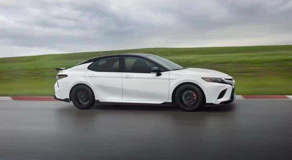 A white 2023 Toyota Camry TRD is shown driving on a racetrack near grass.
