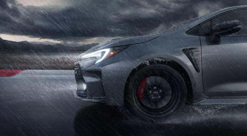 A close-up of the front of a grey 2023 Toyota GR Corolla is shown in the rain.