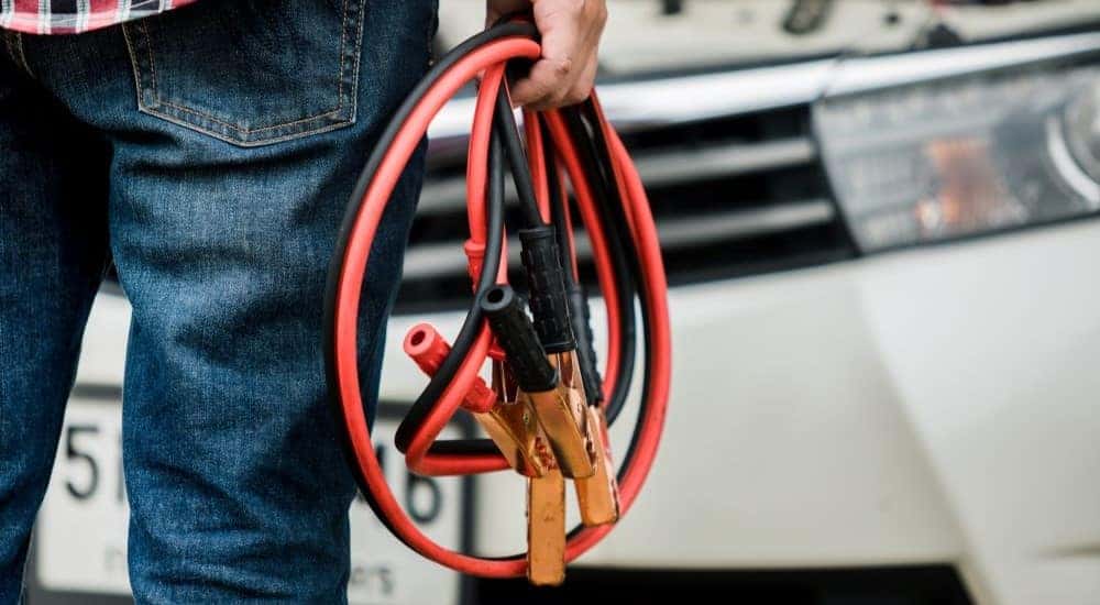 A close up shows a person holding jumper cables.