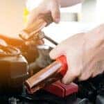 A person is shown using jumper cables before a battery replacement near you.