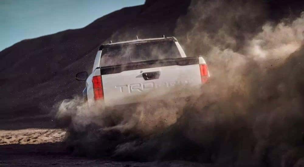 A white 2024 Toyota Tacoma TRD Pro is shown kicking up dust after looking at a Toyota Tacoma for sale.