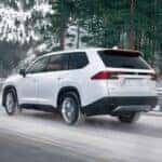 A white 2024 Toyota Grand Highlander is shown driving on a snowy road using snow tires.