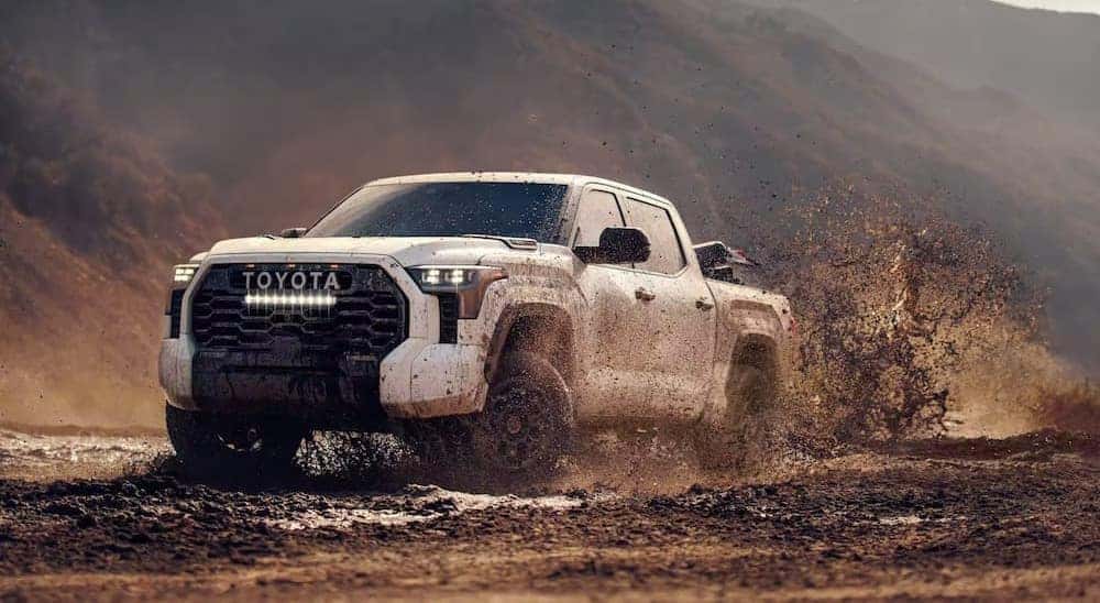 One of many popular Toyota trucks for sale, a white 2024 Toyota Tundra, is shown driving on mud.