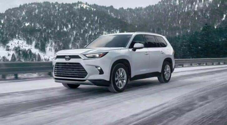 A white 2024 Toyota Grand Highlander is shown driving on a snow covered road.