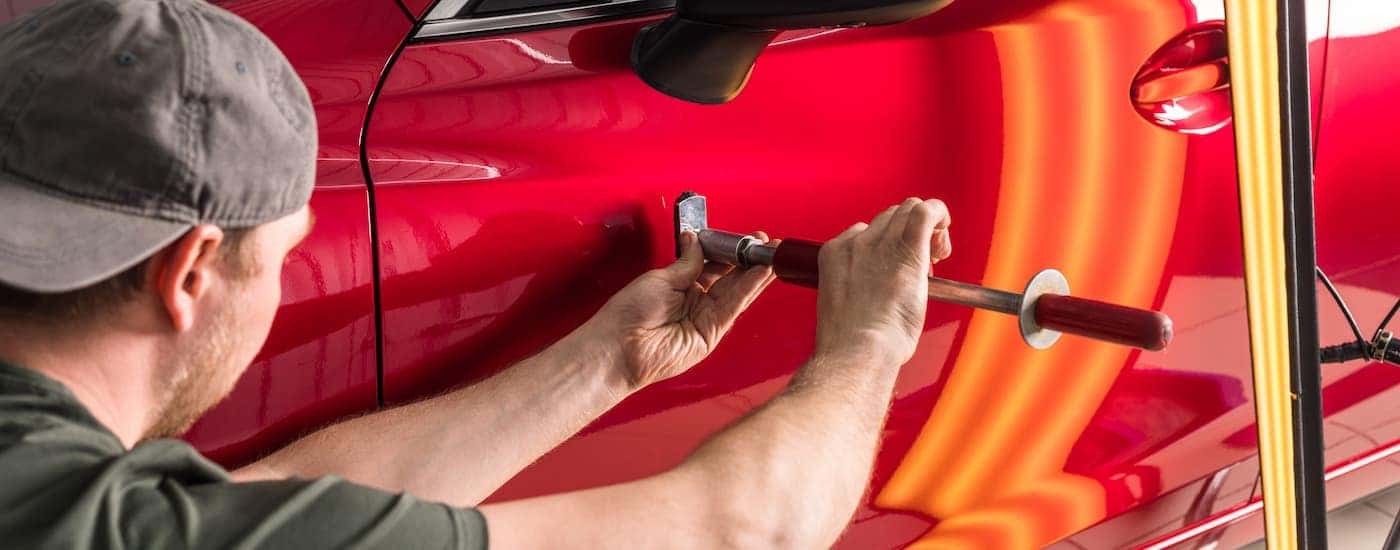 A mechanic is shown removing a dent from a door on a red vehicle.