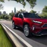 A red 2024 Toyota RAV4 Prime is shown driving to an Oswego Toyota dealer.