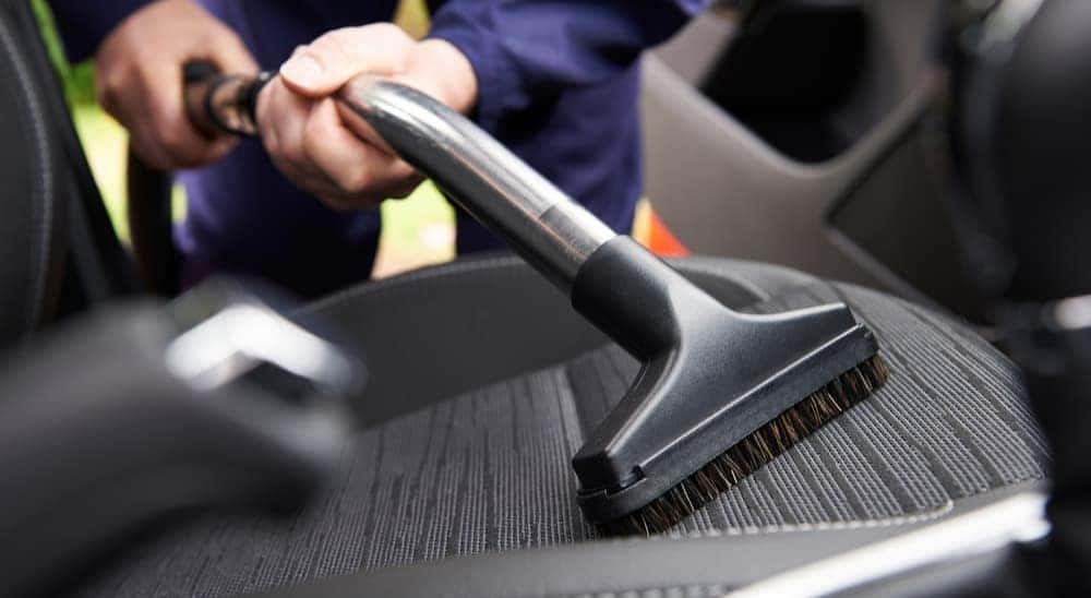 A person is shown vacuuming the interior of a vehicle.