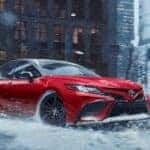 A red 2020 Toyota Camry is shown from the front while driving through snow.