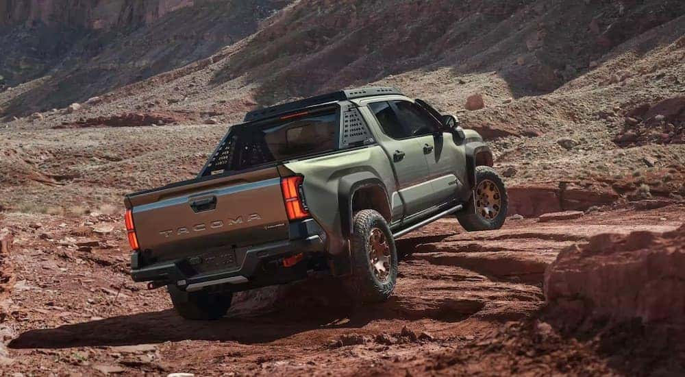A green 2024 Toyota Tacoma Trailhunter is shown from the rear at an angle while crawling over rocks.