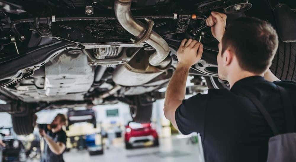 Two mechanics are show working underneath a vehicle.