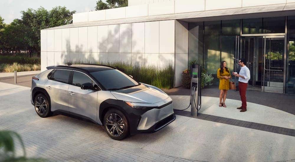 A silver 2024 Toyota BZ4x is shown charging near a building.